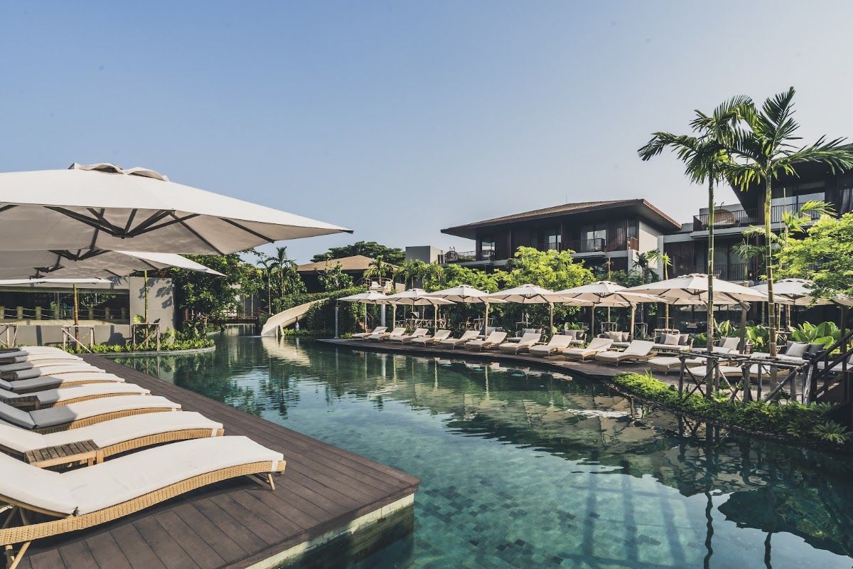 Andaz Pattaya Jomtien Beach resort pool area — sun loungers along a large lagoon pool lined with tropical greenery and resort pavilions