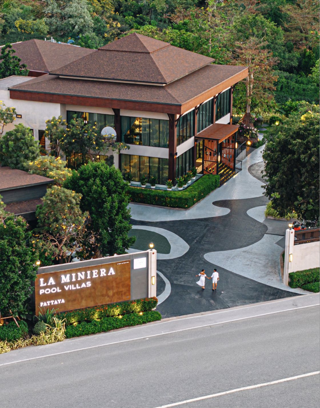 Aerial view of La Miniera Pool Villas Pattaya — resort entrance with lush tropical gardens and a couple walking the winding driveway